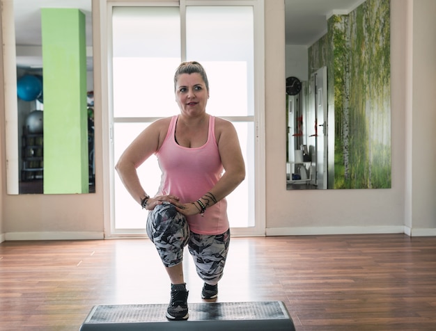 Blonde vrouw in sportkleding doet splits aan de voorkant met een stepper in een kamer