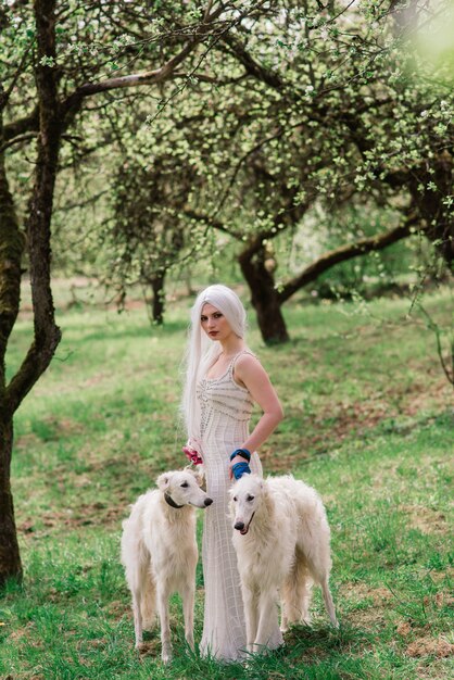 Blonde vrouw in witte jurk spelen met haar Russische wolfshond hond in de tuin.