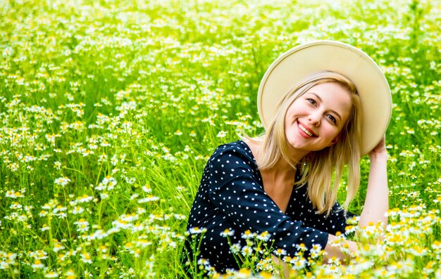 Blonde vrouw in zwarte jurk zittend op chamomiles bloemen veld