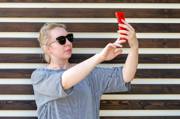 Blonde vrouw maakt selfie of communiceert via video-oproep op de telefoon, tegen de achtergrond van de muur