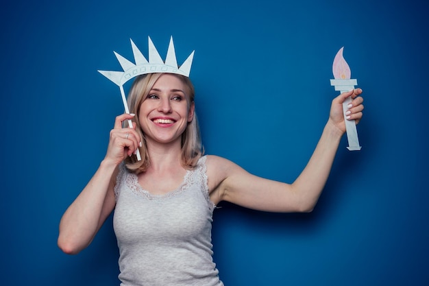 Blonde vrouw met Amerikaanse vlag met papieren kroon en toorts Vrijheidsbeeld op een blauwe achtergrond in de studio 4 juli onafhankelijkheidsdag viering concept en het leren van de Engelse taal