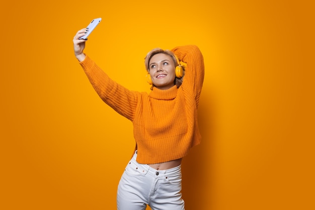 blonde vrouw met gele trui koptelefoon dragen een selfie maken op een muur