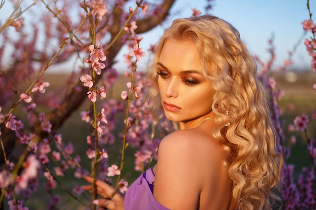 blonde vrouw met golvend haar poseren met bloeiende perzikbomen tegen de hemel