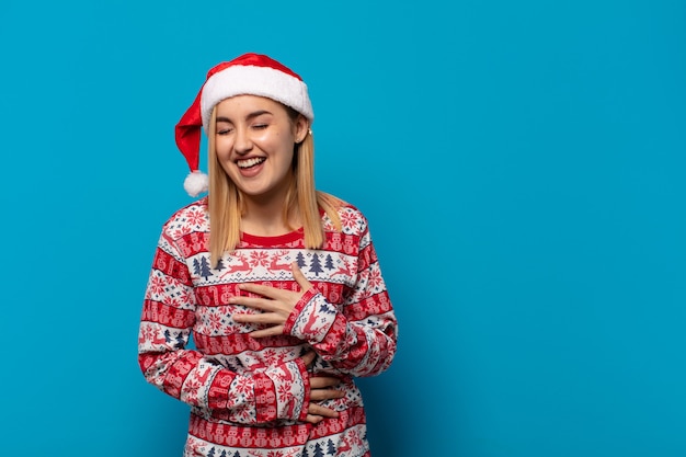 Blonde vrouw met kerstmuts die hardop lacht om een of andere hilarische grap, zich gelukkig en opgewekt voelt, plezier heeft