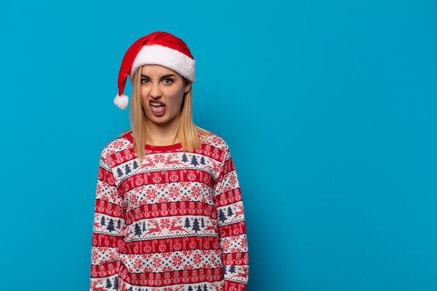 Blonde vrouw met kerstmuts walgt en geïrriteerd, steekt tong uit, houdt niet van iets smerigs en vies