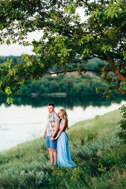 Blonde vrouw met los haar in een lichtblauwe jurk en een man in het licht van de zonsondergang in de natuur