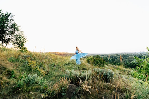 Blonde vrouw met los haar in een lichtblauwe jurk en een man in het licht van de zonsondergang in de natuur