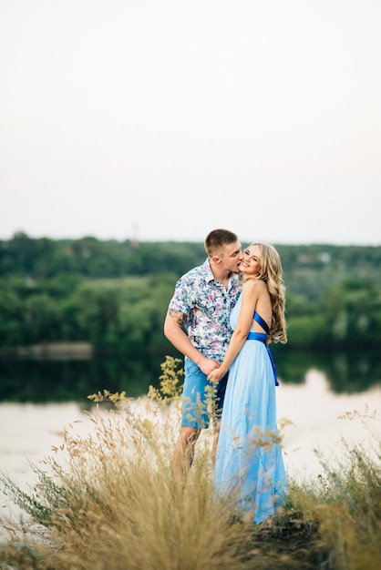 Blonde vrouw met los haar in een lichtblauwe jurk en een man in het licht van de zonsondergang in de natuur