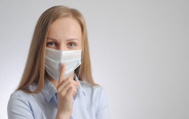 Foto blonde vrouw met medisch masker toont stilte en wees stil gebaar