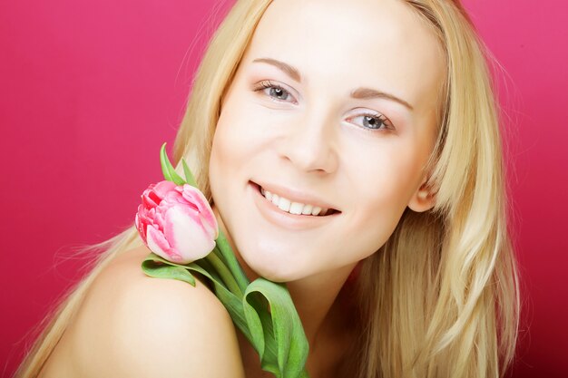 Foto blonde vrouw met roze tulp over roze achtergrond