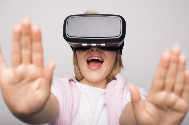 Blonde vrouw met virtual reality headset op hoofd is emotioneel op witte muur