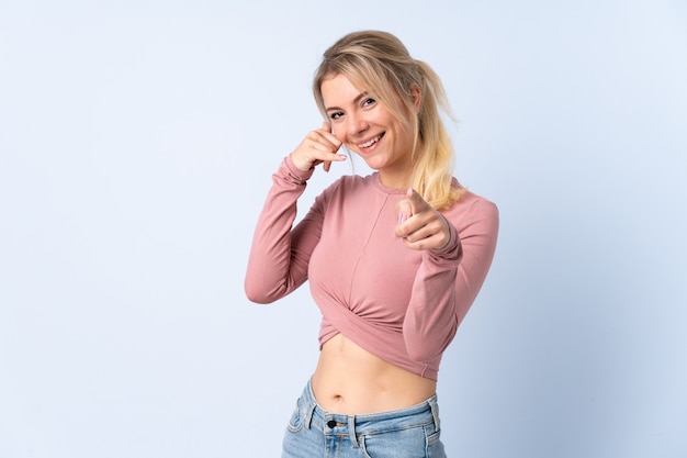 Blonde vrouw over geïsoleerd blauw telefoongebaar maken en naar voren wijzen