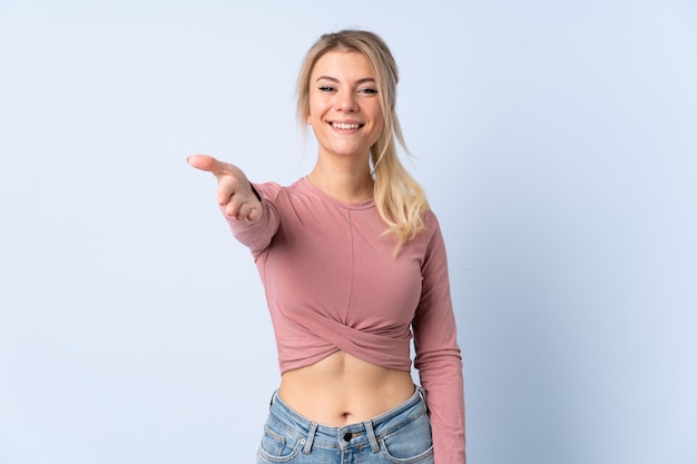 Blonde vrouw over geïsoleerde blauwe achtergrond handen schudden voor het sluiten van een goede deal