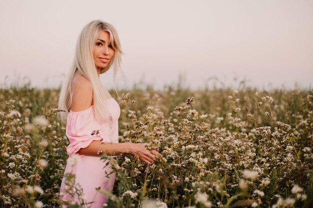 Blonde vrouw poseren in het grote eindeloze veld van madeliefjes in de zomeravond