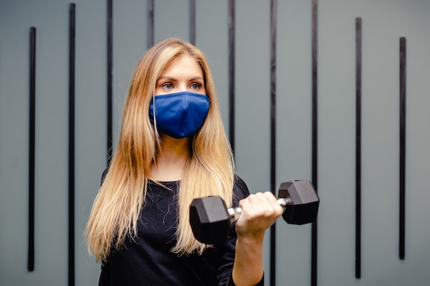 Blonde vrouw traint in de sportschool tijdens de pandemie. Het meisje doet oefeningen in medisch masker