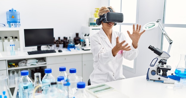 Foto blonde vrouw van middelbare leeftijd, gekleed in een wetenschapperuniform met een vr-bril die in het laboratorium werkt