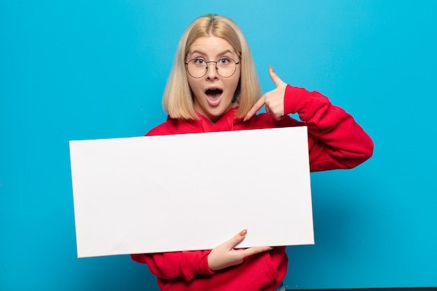 Blonde vrouw voelt zich blij, verrast en trots, wijst naar zichzelf met een opgewonden, verbaasde blik