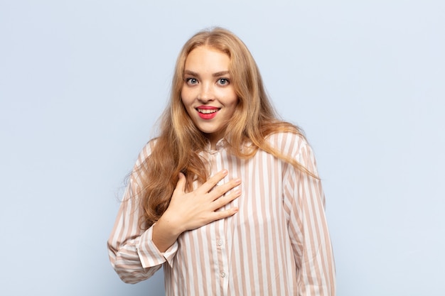 Blonde vrouw voelt zich geschokt en verrast, glimlacht, hand in hand, blij om degene te zijn of dankbaarheid te tonen