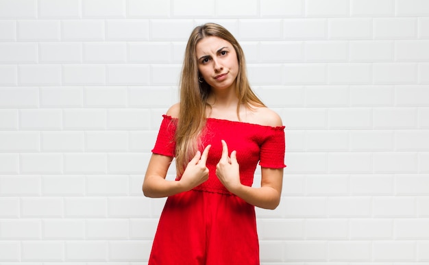 Foto blonde vrouw wijzend naar zichzelf met een verwarde en vragende blik, geschokt en verrast om gekozen te worden