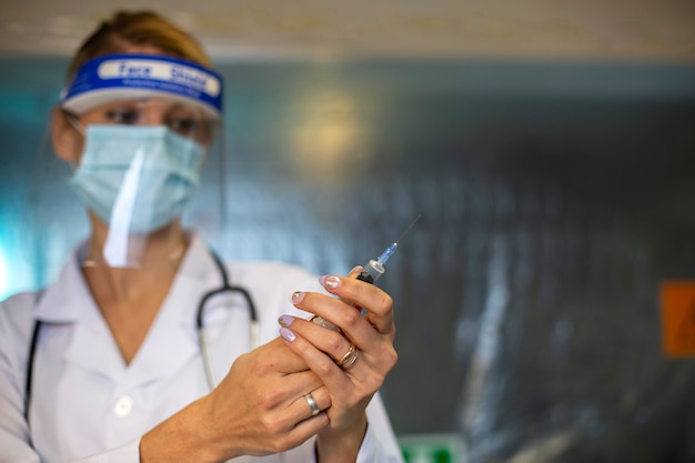Blonde vrouwelijke arts met beschermend masker klaar om de angel voor virusgriep te doen. Vaccin