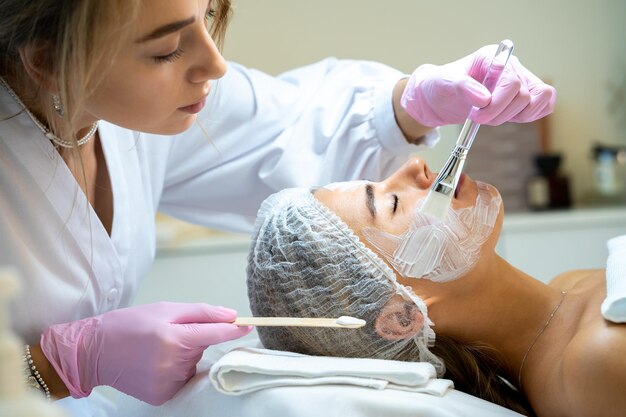 Blonde vrouwelijke cosmetoloog die een masker op het gezicht aanbrengt in een esthetische kliniek cosmetische behandeling
