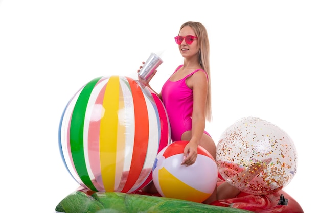 Blonde vrouwen in een roze badpak zitten op een luchtbed met kleurrijke strandballen