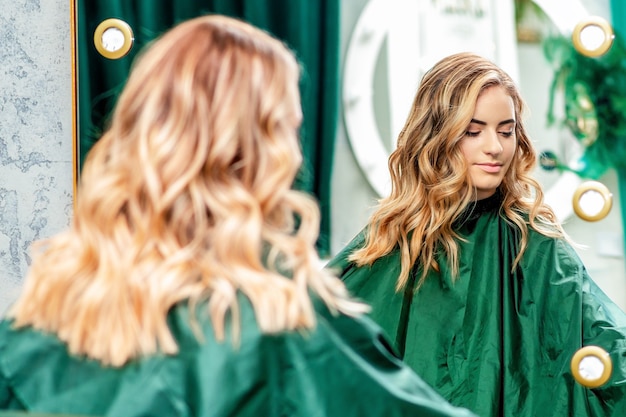 Blonde wavy hairstyle of young woman in the mirror at beauty salon