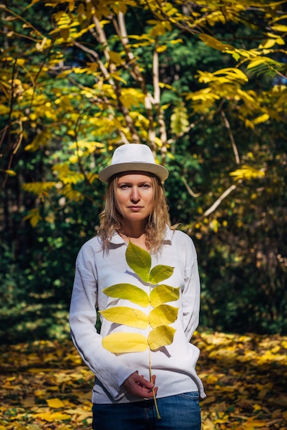 Photo blonde in white shirt and hat walks in beautiful park on sunny autumn day. harmony with nature, the benefits of vitamin d.