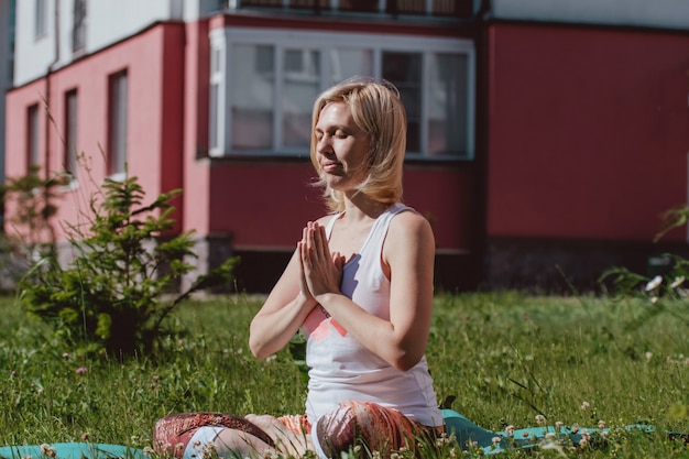 Blonde in a white t-shirt on the green grass doing yoga. Treatment and relaxation of the spine. Sports lifestyle