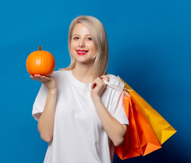 Blonde in white t-shirt with shopping bags and pumpkin on blue space