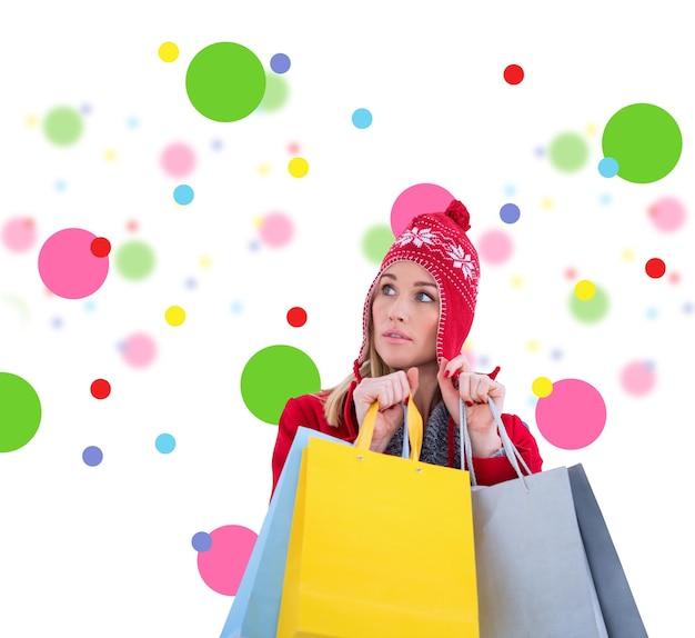 Blonde in winter clothes holding shopping bags against dot pattern