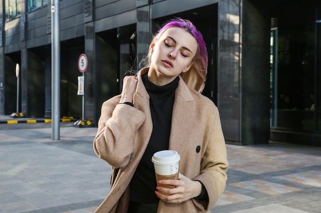 blonde with lilac strands of hair in a beige coat with a cup of coffee