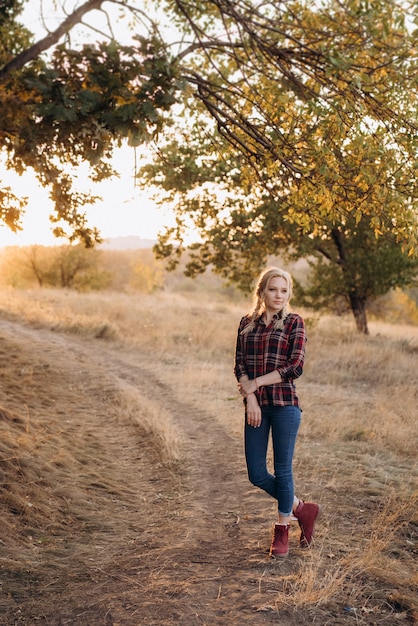 Bionda con le trecce in camicia, jeans, scarpe rosse che sorride al tramonto