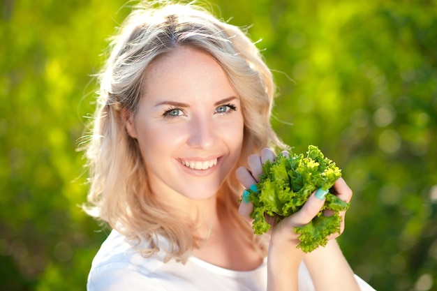 Блондинка 20-22 лет держит салат на фоне природы. Здоровый образ жизни. Молодые взрослые.