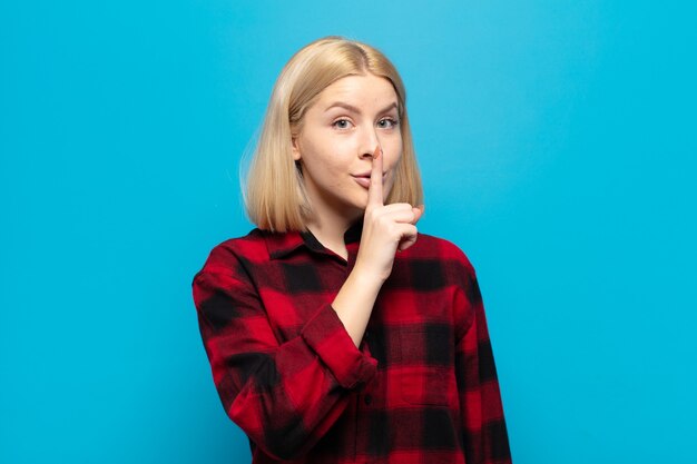 Blonde woman asking for silence and quiet, gesturing with finger in front of mouth, saying shh or keeping a secret