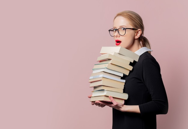 Blonde woman in black dress with books on pink 