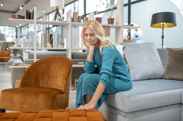 Blonde woman in a blue dress touching the sofa