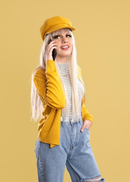 Blonde woman in cap and yellow jacket talking on the phone on yellow background