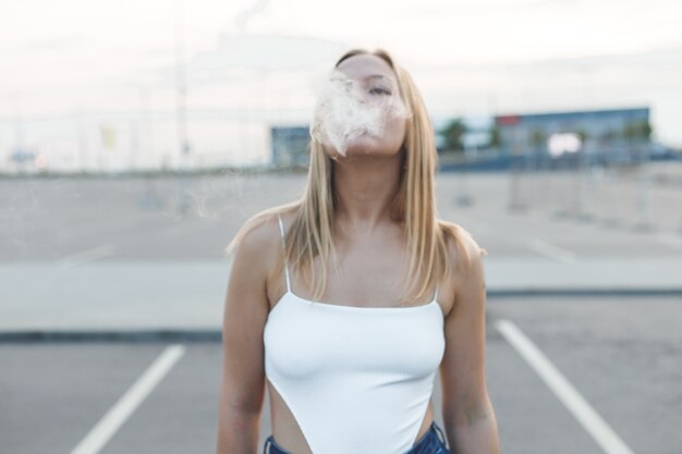 電子タバコvapingと都市のブロンドの女性