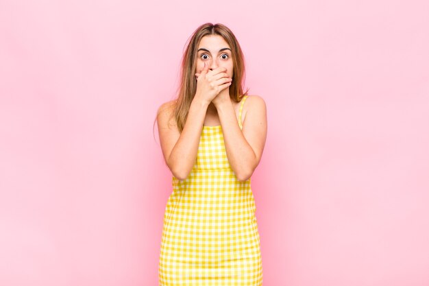 Blonde woman covering mouth with hands with a shocked, surprised expression, keeping a secret or saying oops