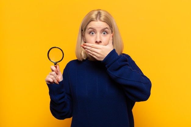 Photo blonde woman covering mouth with hands with a shocked, surprised expression, keeping a secret or saying oops