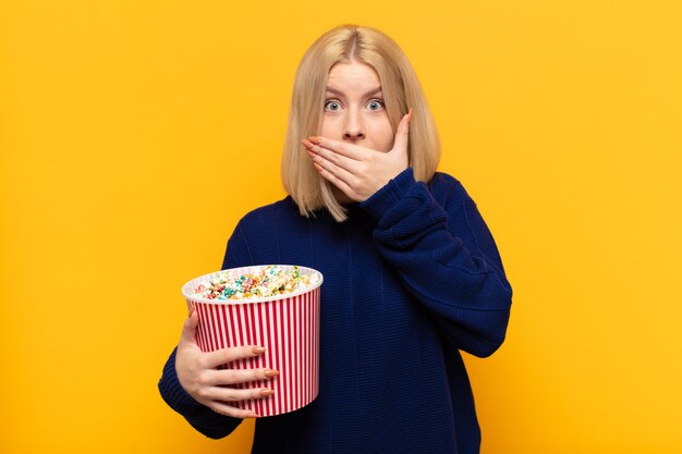 Blonde woman covering mouth with hands with a shocked, surprised expression, keeping a secret or saying oops