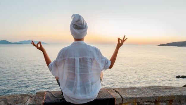 Blonde woman doing breathing pranayama exercise on sunset on the sea. .