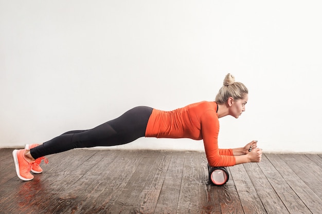 Blonde woman doing plank in foam roller. Studio shot