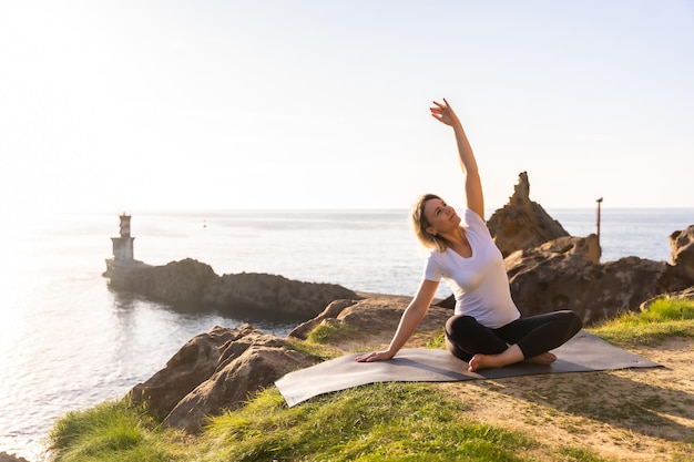 A blonde woman doing yoga exercises in nature by the sea doing stretching
