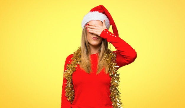 Blonde woman dressed up for christmas holidays covering eyes by hands.