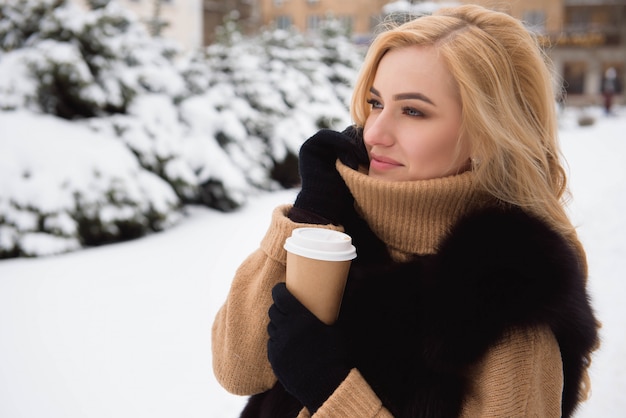 冬の公園でコーヒーを飲みながらブロンドの女性