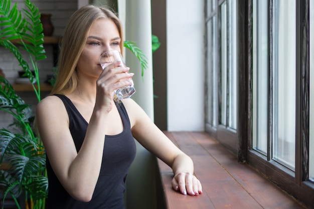 A blonde woman drinks water from a glass. concept of water use for women