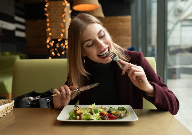 blonde woman eating green healthy tasty eco salad on city cafe