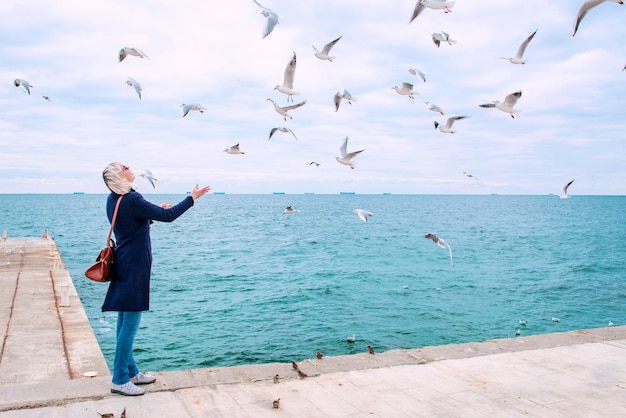 blonde woman feeding seagulls in cloudy autumn day on the sea coast